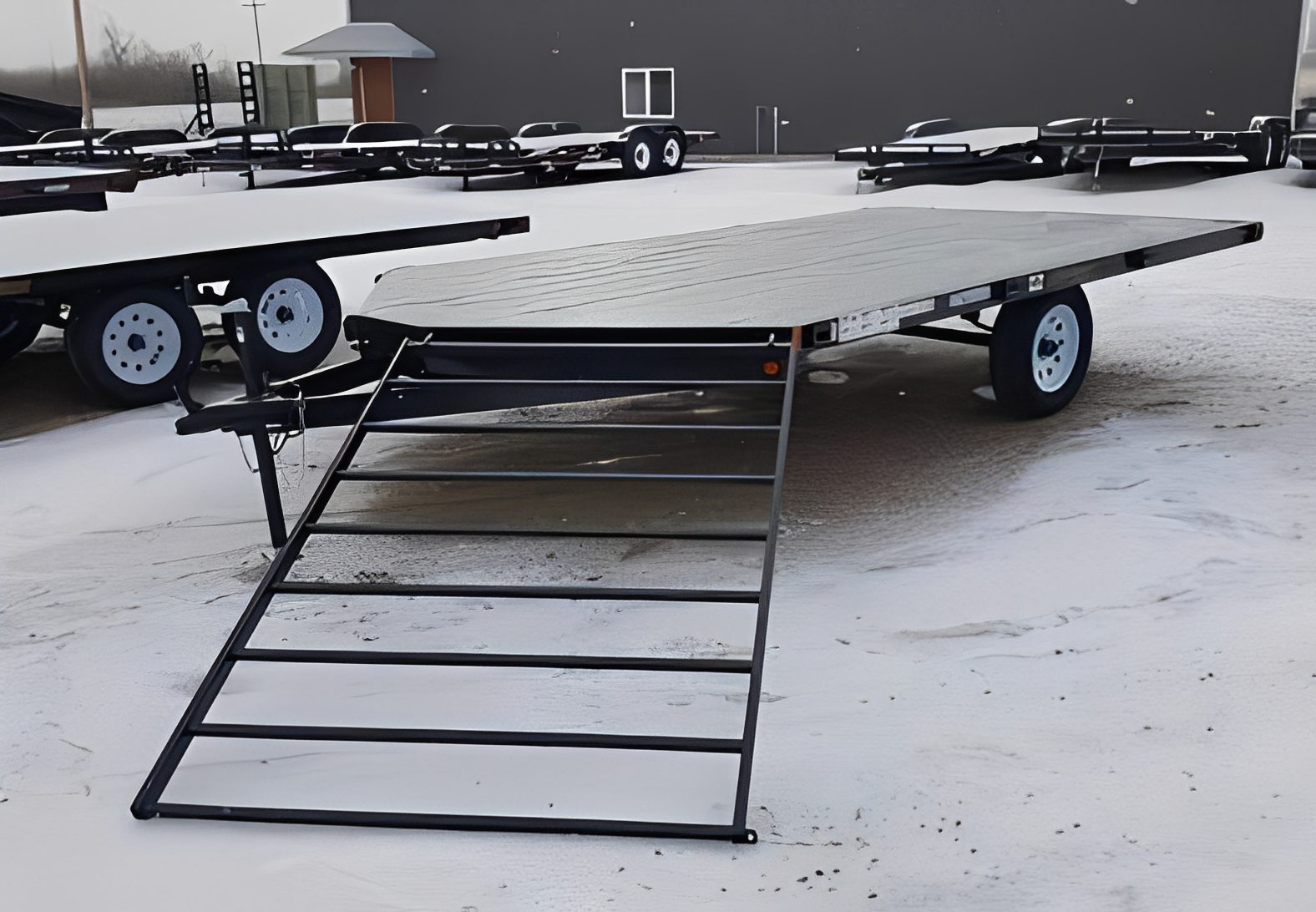 Flatbed trailer with ramp in snowy lot.