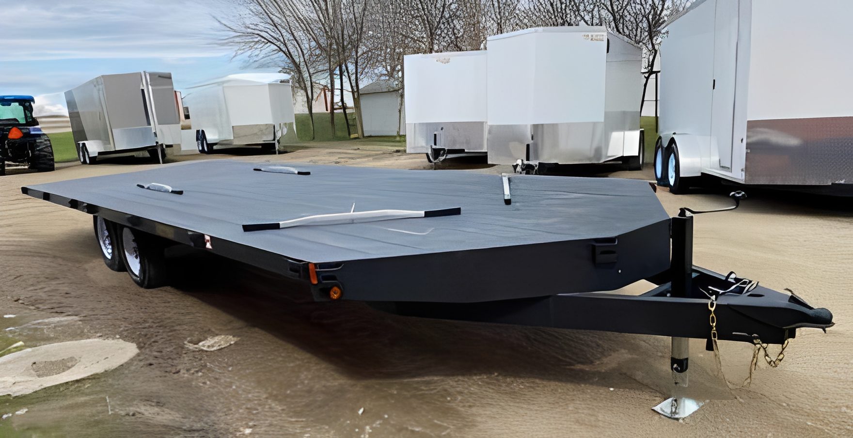 Black flatbed trailer near white trailers